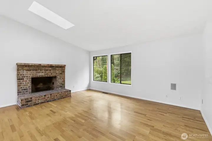 Spacious living room featuring a wood-burning fireplace, large picture windows, and two skylights that fills the space with natural light.