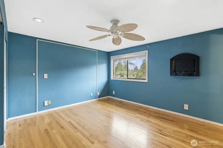 Primary bedroom view highlights a ceiling fan and a wall fireplace that creates the illusion of a real fire.