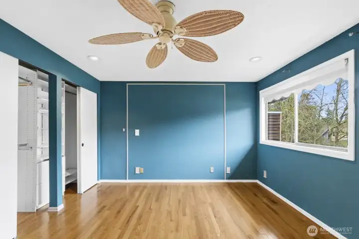 Bright primary bedroom with closet built-ins and a large picture window that welcomes abundant sunlight.