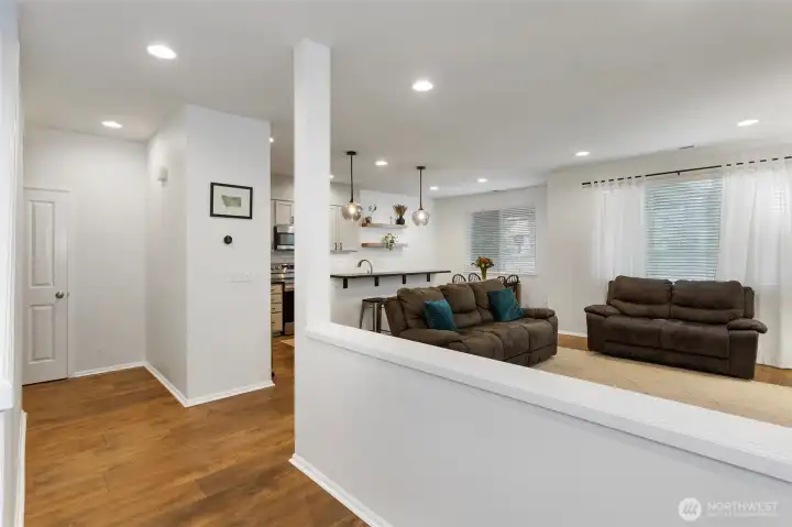 Open and airy entry view highlighting warm LVP floors, recessed lighting, and a smooth transition into the main living area. The partial wall creates subtle separation while maintaining an open-concept flow, offering a clear sightline to the living room and kitchen beyond.