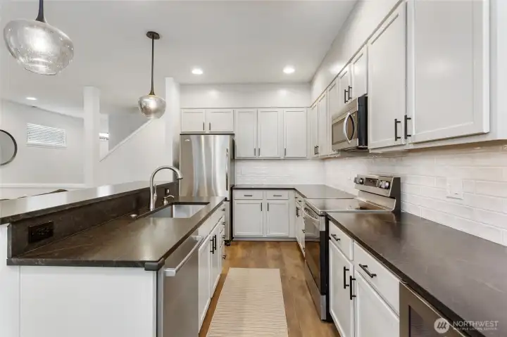Stylish open kitchen featuring durable LVP flooring and elegant granite countertops that extend across the peninsula for added prep and seating space. Updated cabinetry, stainless steel appliances, and a classic subway-tile backsplash are complemented by modern pendant lighting, creating a bright, functional kitchen that flows seamlessly into the main living area.