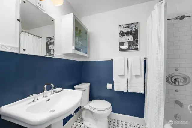 Fully remodeled bathroom, a crisp navy and white, features pedestal sink, vintage tile floors, new fixtures and full tub/shower combination with subway tile.