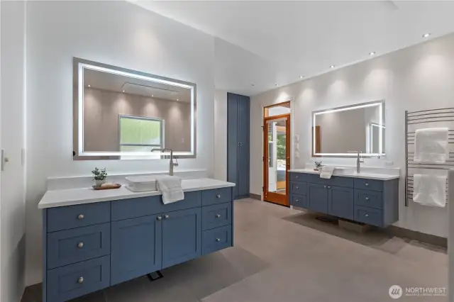 The double vanities have lighted vanity mirrors with defogging features. there is an entrance to the pool patio from the primary bath