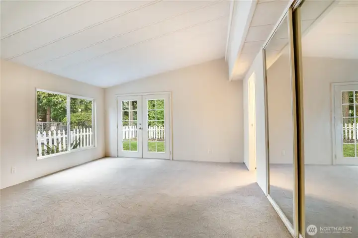 The primary bedroom feels airy and inviting with vaulted ceilings and French doors that open to a private, tree-lined backyard.