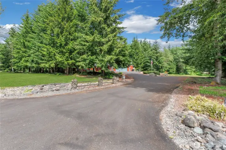 Rock lined asphalt driveway, home on left, shop on the right