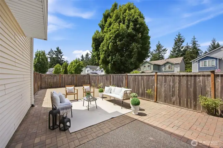 Fully fenced back patio with brick pavers and berry and rose bushes surrounding.