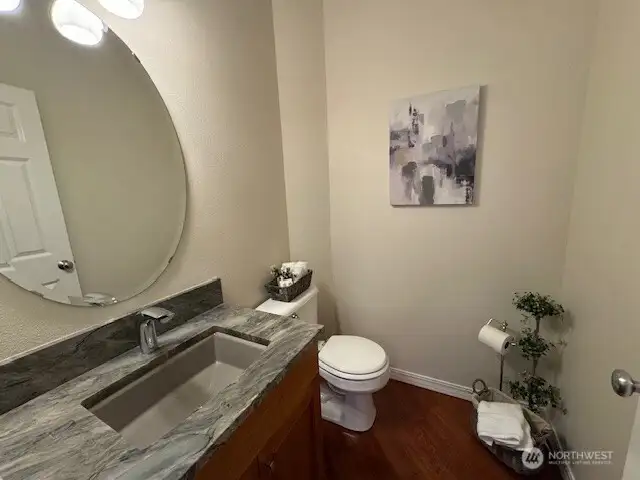 Modernized half bath featuring a stunning stone countertop, seamlessly complemented by the continuation of rich cherry hardwood floors for a cohesive and stylish look.
