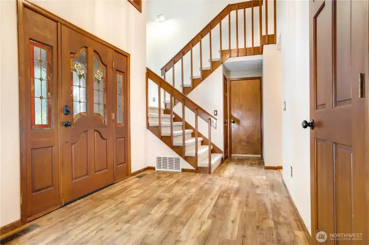 Welcoming two-story foyer with rich wood entry doors, open staircase, and low-maintenance plank flooring that sets the tone for this warm Northwest home.