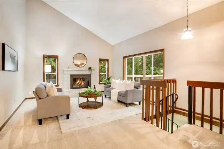 Sunny vaulted family room with a painted brick fireplace, large picture window, and glass doors to the deck—an inviting hub that connects cozy evenings inside with outdoor living.