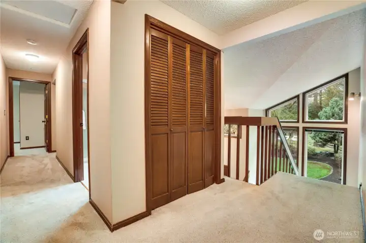 Open upstairs hallway with extra storage and a dramatic overlook to the vaulted entry windows, connecting the primary suite and three additional bedrooms.