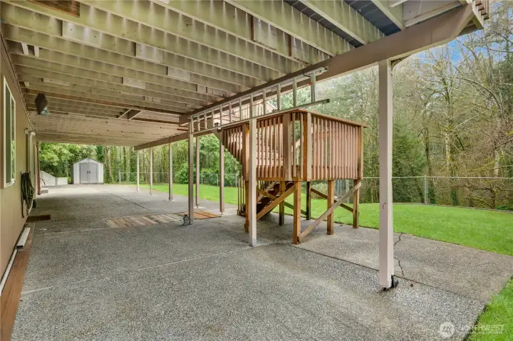 Covered lower patio under the deck with plenty of space for outdoor dining, ping-pong, or a future hot tub, all overlooking the huge grassy yard and trees.