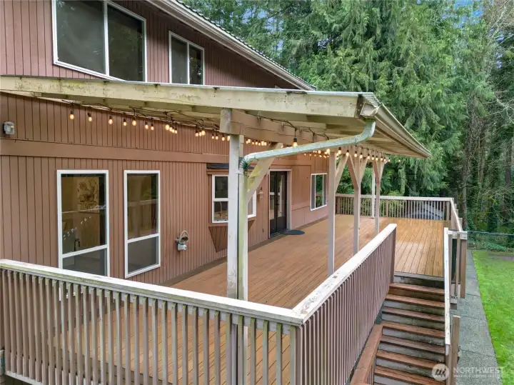 Wraparound covered deck with string lights and wooded views—your year-round outdoor living room with plenty of space for lounging, dining, and grilling.