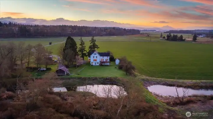 This incredible aerial view shows exactly what 'massive privacy' looks like here in Stanwood. Tucked at the end of a 1,600-foot private drive, this historic 1890 farmhouse has been a sanctuary for only four owners over the last 136 years, and it’s easy to see why. The home is perched on a significant elevated building pad for peace of mind, offering a front-row seat to 316 feet of Port Susan waterfront where Trumpeter Swans, eagles, and river otters are your only neighbors. You’re looking at a true legacy estate that blends sustainable living—complete with its own orchard and gardens—with the rare convenience of being just minutes from downtown shopping and I-5. It’s a peaceful, once-in-a-generation retreat that feels worlds away while staying perfectly connected to the community.