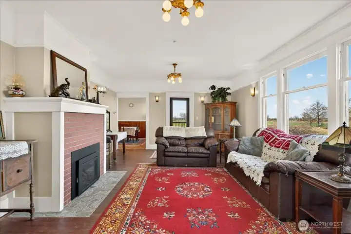 The living room is such a comfortable spot to sit back and take in the views. The brick fireplace adds that classic,  feel you want in an 1890 farmhouse, and the whole room feels bright and welcoming. You can see how it connects right to the dining area, and those large windows look straight out over the backyard with no neighbors in sight. It’s a peaceful and that’s been a central part of this home's 136-year history.