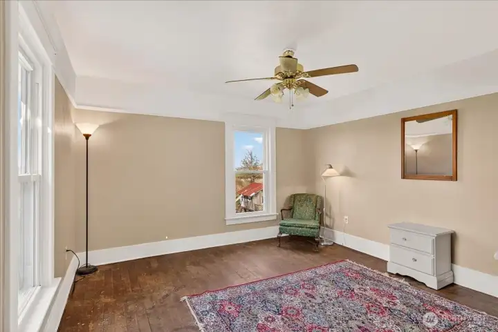 This upstairs bedroom is another bright, open space with plenty of natural light. The windows look right out over the property and the historic outbuildings, giving it a really peaceful feel. With the original hardwood floors and classic white trim, it’s a simple, solid room that keeps that authentic farmhouse character going throughout the top floor.