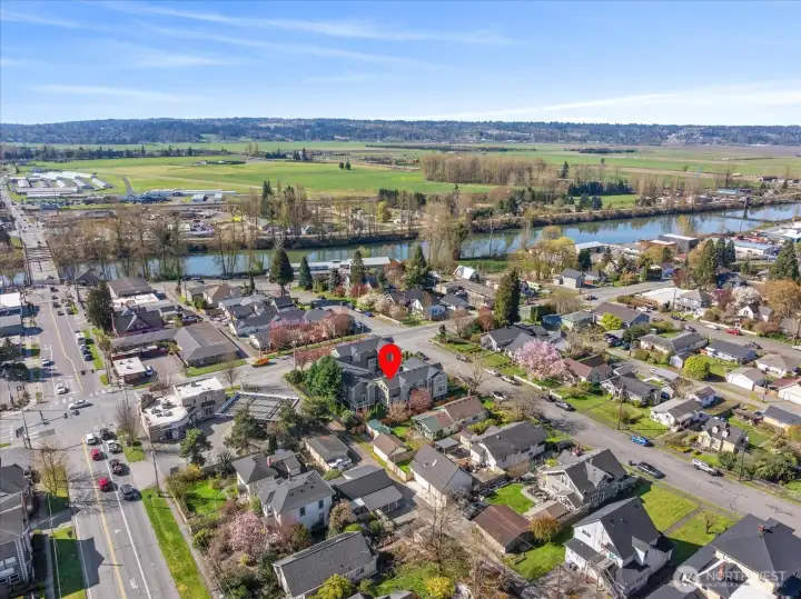 Aerial view of residential neighborhood with property marker, nearby river, and surrounding farmland.