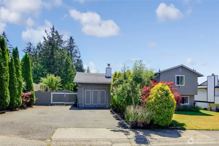 Detached garage with extended driveway, surrounded by mature landscaping and evergreens.