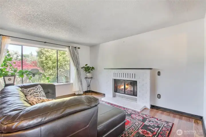 Cozy white brick fireplace framed by a large window with garden views.