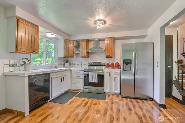 Stainless appliances, wood cabinetry, and tile counters with a garden window.