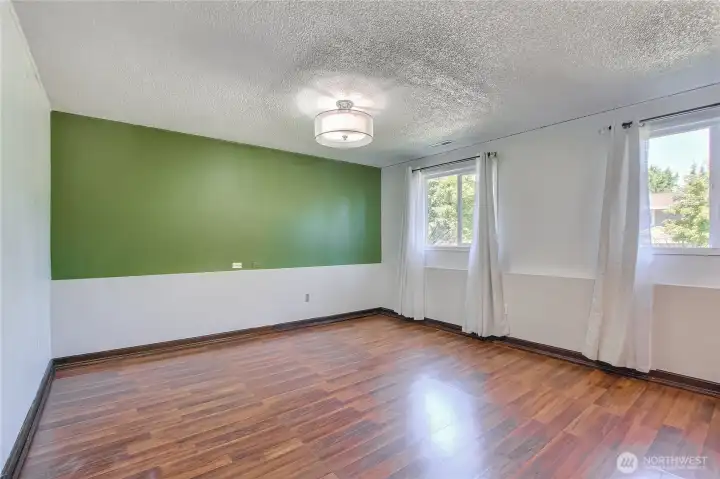Spacious room with green accent wall and rich laminate flooring.