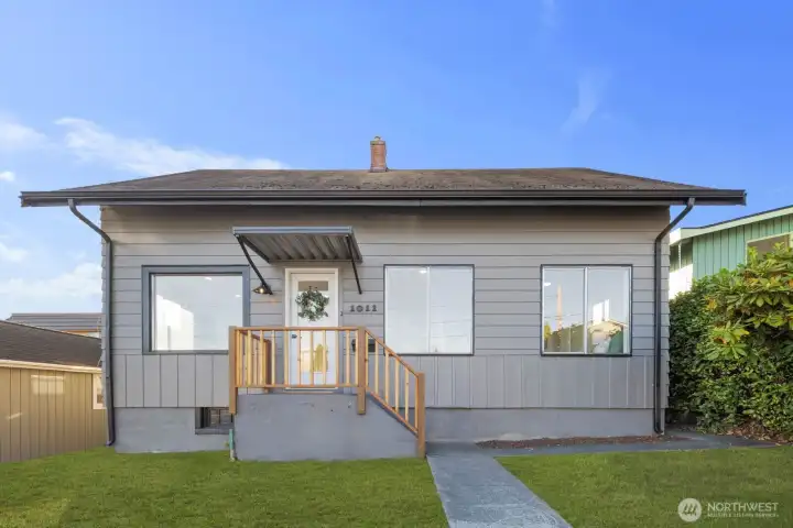 Inviting exterior with horizontal siding, covered entry, and a simple wood-railed porch surrounded by a neatly maintained lawn.