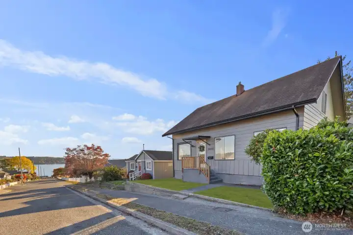 Angled view showing the home’s roofline, front landscaping, and peek toward nearby water and tree-lined surroundings.