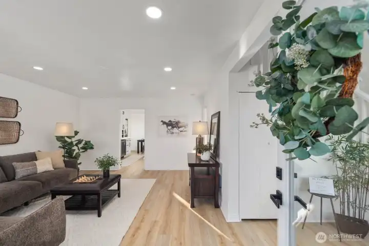 Bright entry leading into an open living area with recessed lighting, light-toned flooring, and a clean, modern aesthetic.
