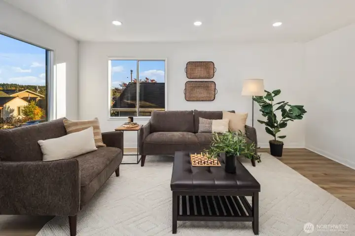 Living room with large picture windows, neutral wall tones, and seating area arranged on a soft woven rug.