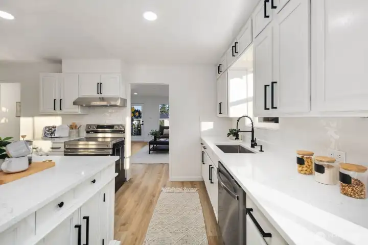 Extended view of the kitchen showcasing abundant cabinet storage, undermount sink with matte black fixtures, and natural light from multiple windows.