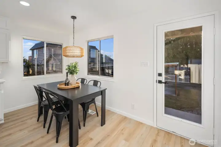 Adjacent dining space with a large window, woven pendant light, and direct access to the backyard through a glass-paneled door.