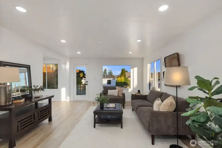 Spacious living area featuring wide-plank flooring, recessed lighting, and large windows that bring in natural light from multiple directions.