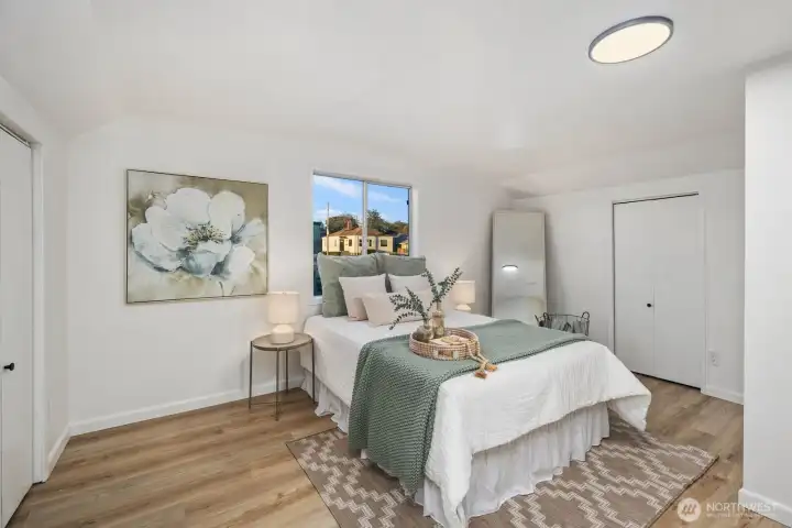 Upstairs bedroom with sloped ceiling detail, neutral color palette, and ample closet space framed by light wood flooring.