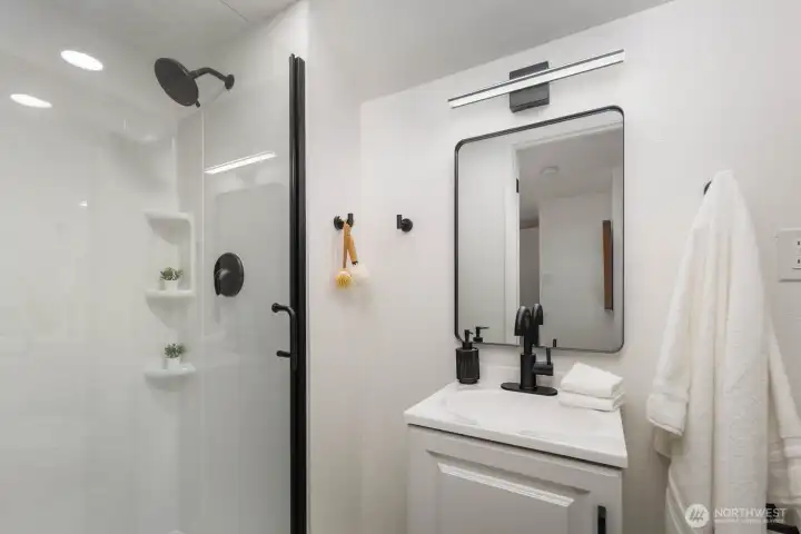 Modern bath with a walk-in shower, glass enclosure, black fixtures, and a white vanity with matching framed mirror.
