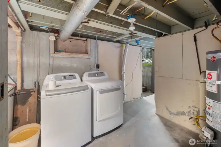 Alternate angle of the lower-level space showing washer and dryer placement, exposed beams, and access to the exterior.