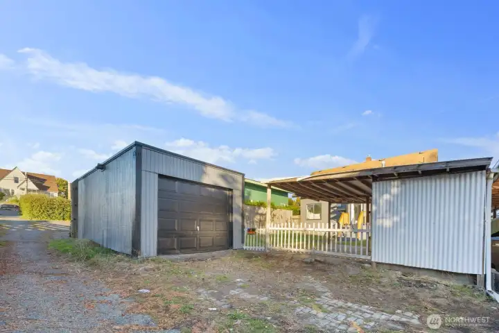 Fenced backyard featuring a level lawn, covered parking area, and steps leading to the home’s rear entry.
