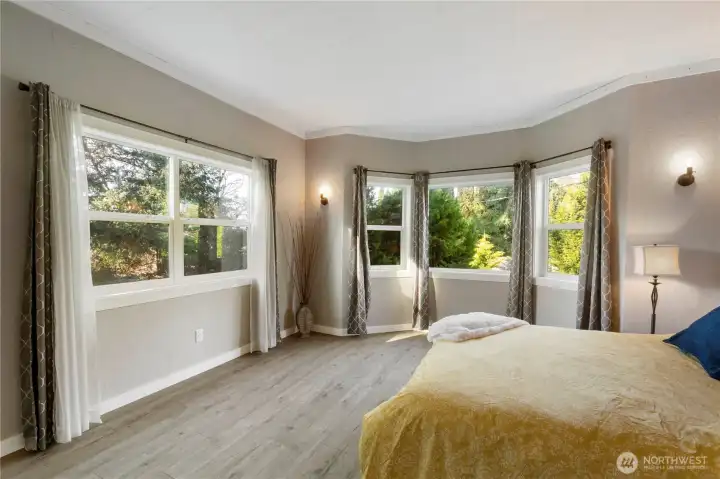 The architectural detail of the bay window is the standout feature in this room, drawing in abundant natural light and framing peaceful, green views outside. Multiple windows wrap the space in daylight throughout the day, creating a bright, uplifting atmosphere that makes this bedroom feel both welcoming and serene.