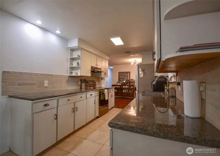 This kitchen features granite countertops, abundant cabinetry, and generous prep space, along with a deep stainless steel sink, all appliances included, and durable tile flooring.
