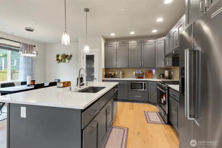 Kitchen with large center island, quartz countertops, and plenty of cabinets.  Notice the beautifu engineered hardwood floors throughout the entire main floor.  Perfect for everyday living and entertaining.