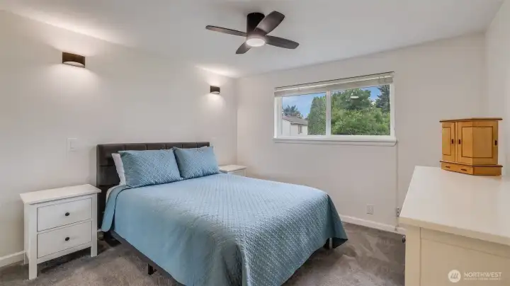 Bright and inviting primary bedroom featuring a large window, modern ceiling fan light and wall sconces, and a serene atmosphere.