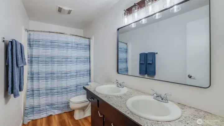 Stylish full bath featuring a dual-sink vanity, updated lighting, and a tub/shower combo.
