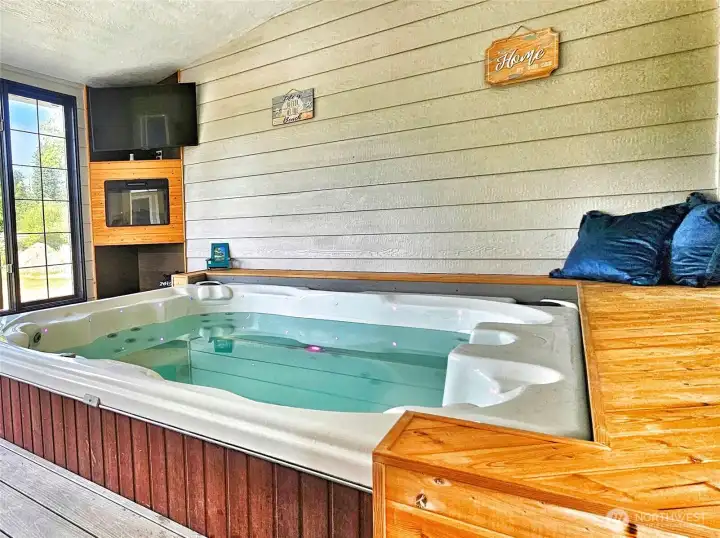 Wood bench surrounding hot tub with entertainment & fireplace.