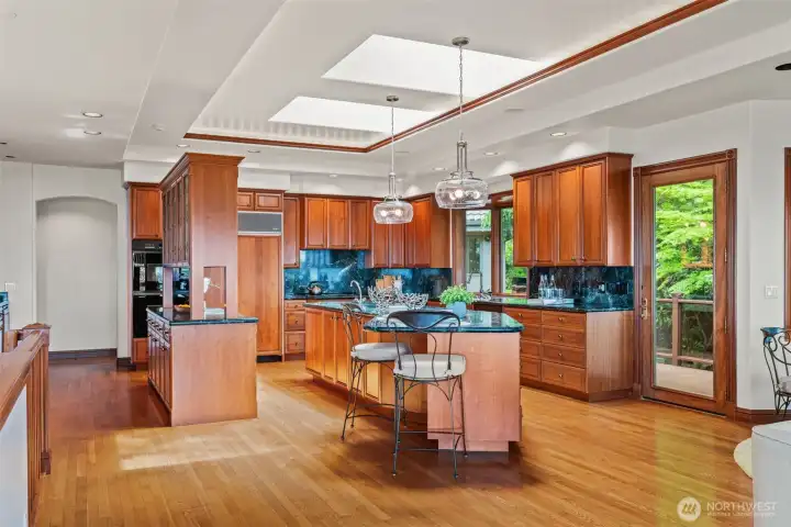 A beautifully designed chef’s kitchen showcasing rich custom cherry cabinetry, extensive millwork, and expansive prep and gathering spaces. Dual islands, skylights, hardwood floors, and walls of custom cabinetry create a warm yet sophisticated setting designed for both everyday living and effortless entertaining. Thoughtful details, abundant storage, and seamless access to outdoor spaces make this kitchen the true heart of the home.
