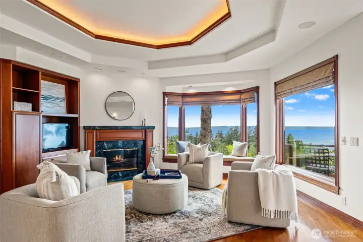 Warm and welcoming, the family room offers the perfect gathering space just off the kitchen, designed for comfortable everyday living and effortless entertaining. Rich custom cabinetry, beautiful millwork, hardwood floors, and a cozy fireplace create an inviting atmosphere, while expansive windows frame peaceful views of Puget Sound and the surrounding landscape.