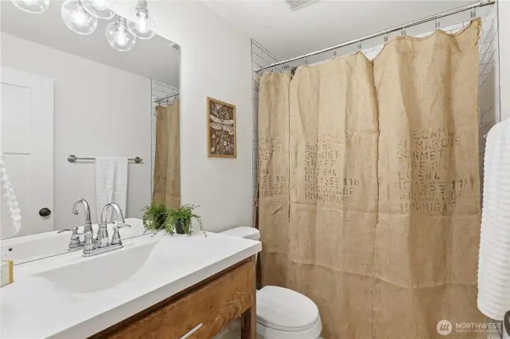 Remodeled bath with timeless penny tile flooring, fresh tile surround, updated vanity, lighting, and fixtures.