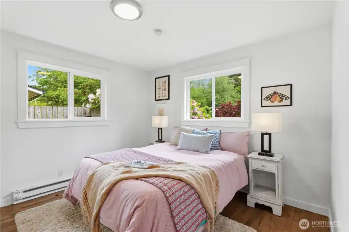 Bright bedroom featuring two windows, hardwood floors, and fresh new paint.