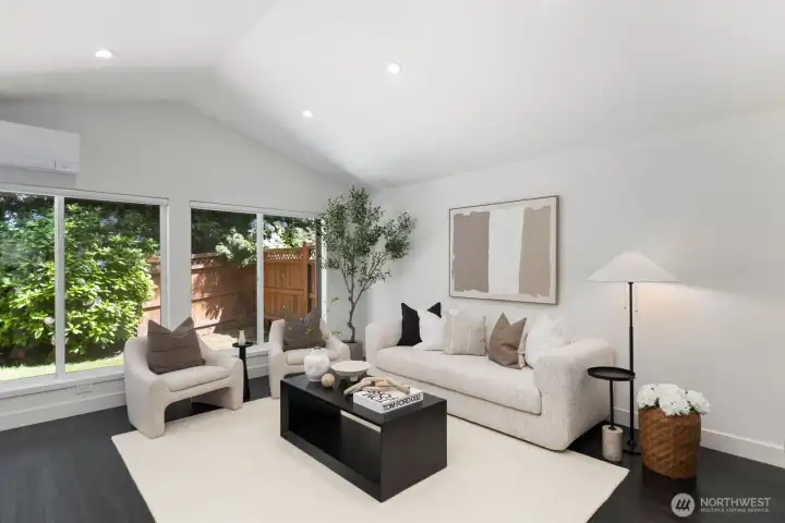 Soaring vaulted ceilings highlight the great room, complemented by ample recessed lighting, a wood-burning fireplace, a built-in bar area, and gleaming floors throughout.