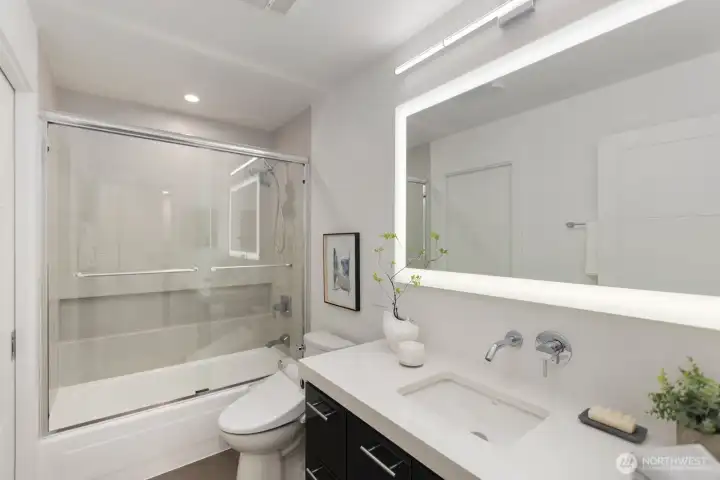 The secondary bath features an en suite layout with dual access for guests, showcasing stunning quartz countertops, a high-end toilet, and specialty lighting.