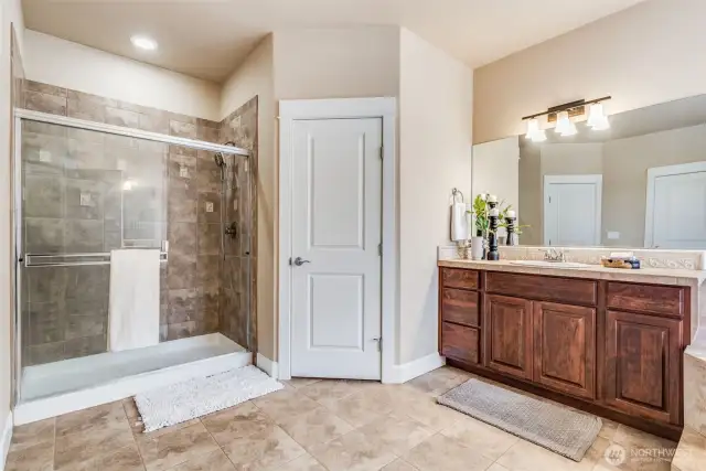 The luxe ensuite features a tile-surround walk-in shower with glass doors, ceramic tile flooring, and dual walk-in closets—each perfectly positioned on either side of the vanities for ultimate convenience and style.
