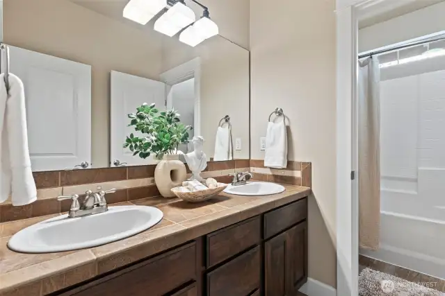 The guest bath features dual sinks, warm tile countertops, and a separate commode & shower/tub combo.