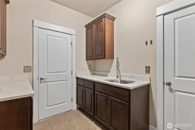 Well-appointed main-level laundry room with deep SS utility sink, quartz counters/backsplash, abundant cabinetry and access to the 3-car garage.